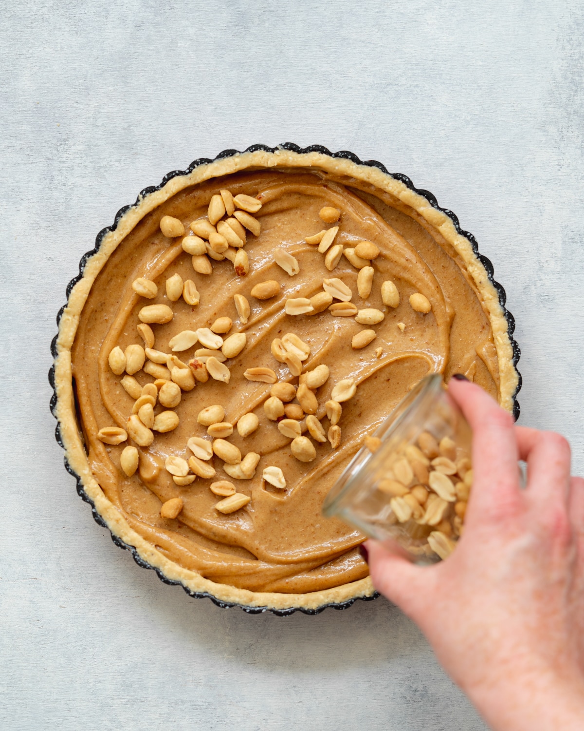 pouring roasted peanuts on top of caramel in a tart base.
