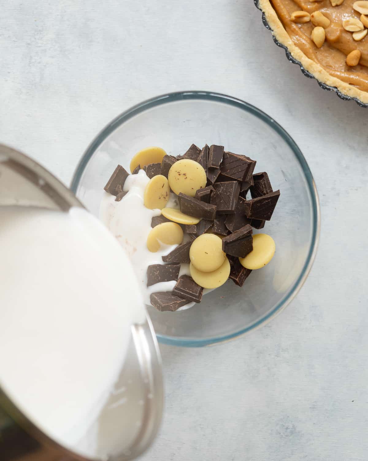 pouring hot coconut milk into a bowl with chocolate and cocoa butter.