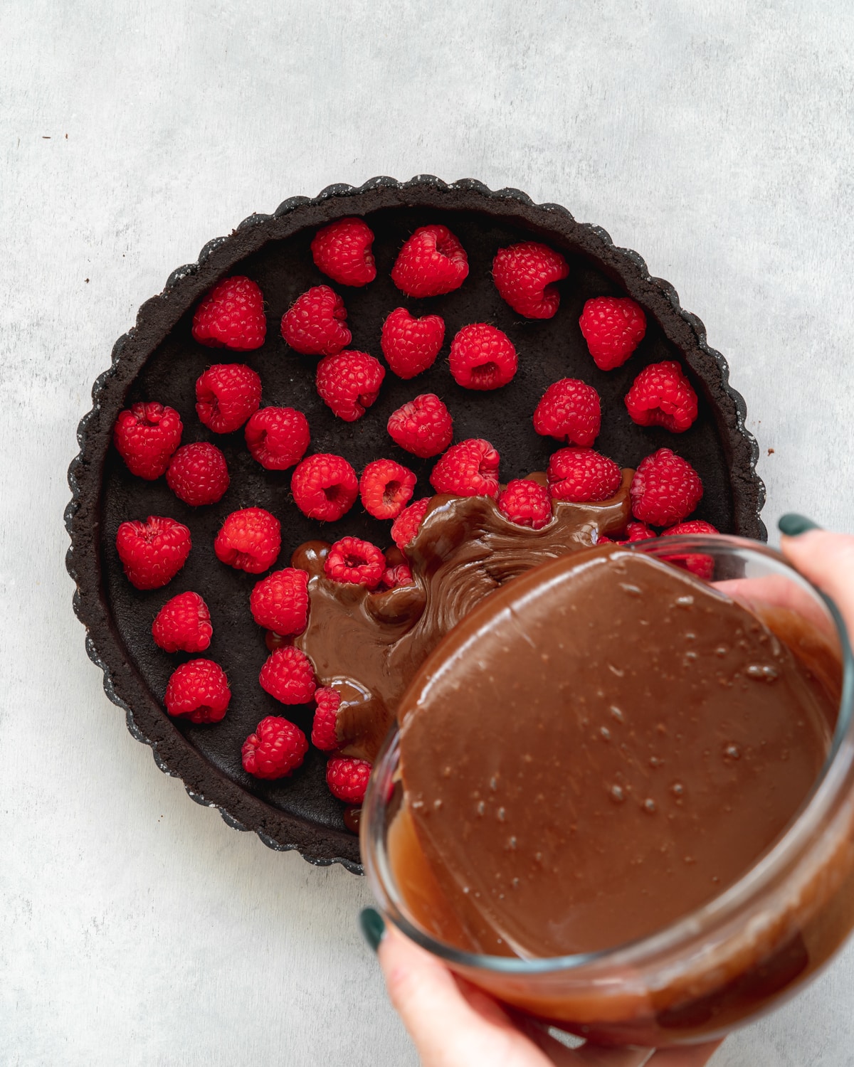 pouring chocolate filling into a tart tin with fresh raspberries.