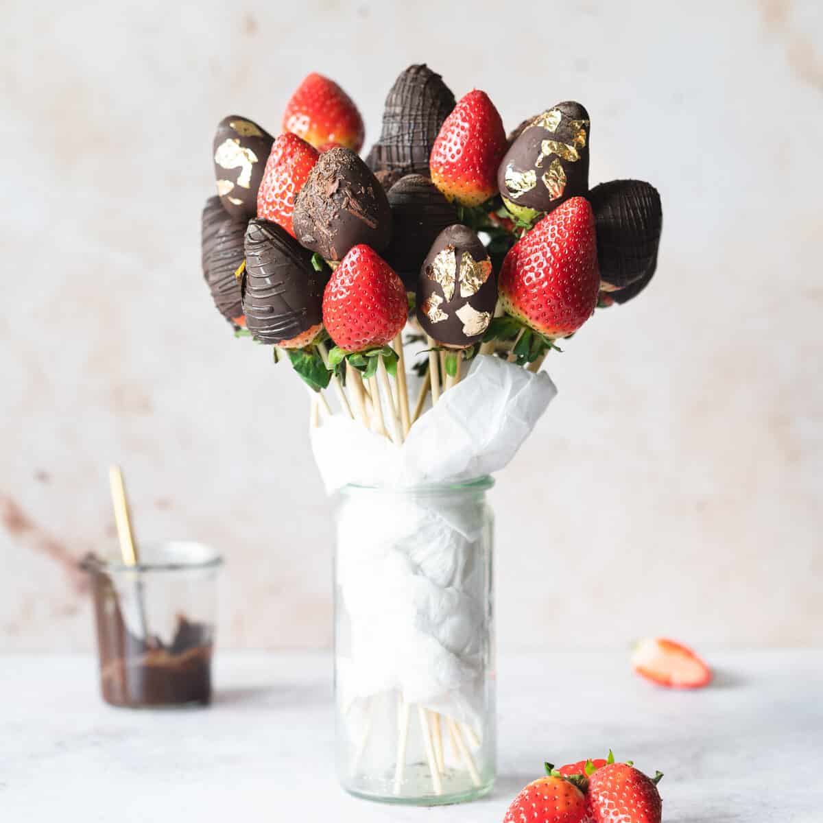 bouquet of chocolate dipped strawberries in a vase against pink background.