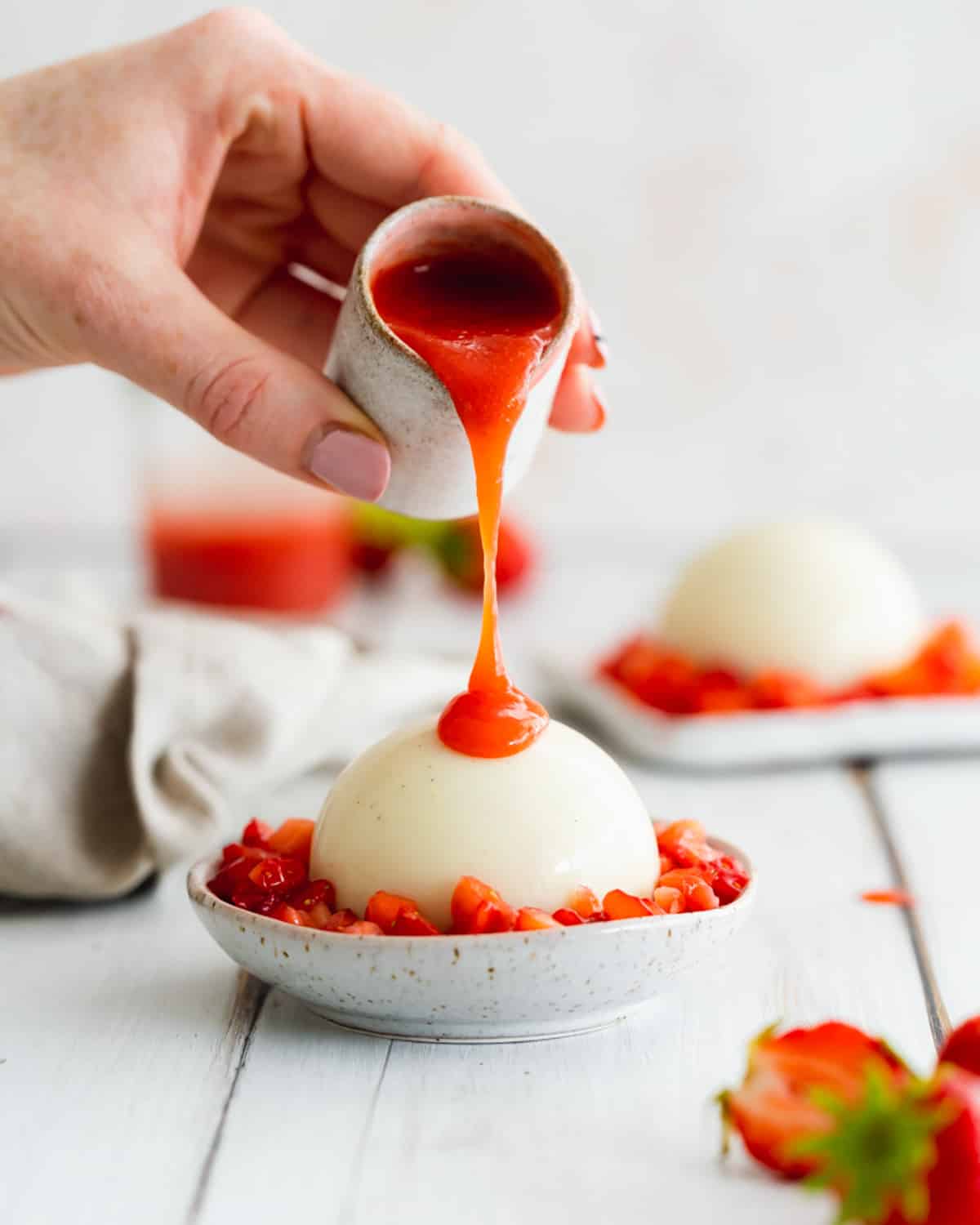 pouring strawberry sauce over dairy free panna cotta.