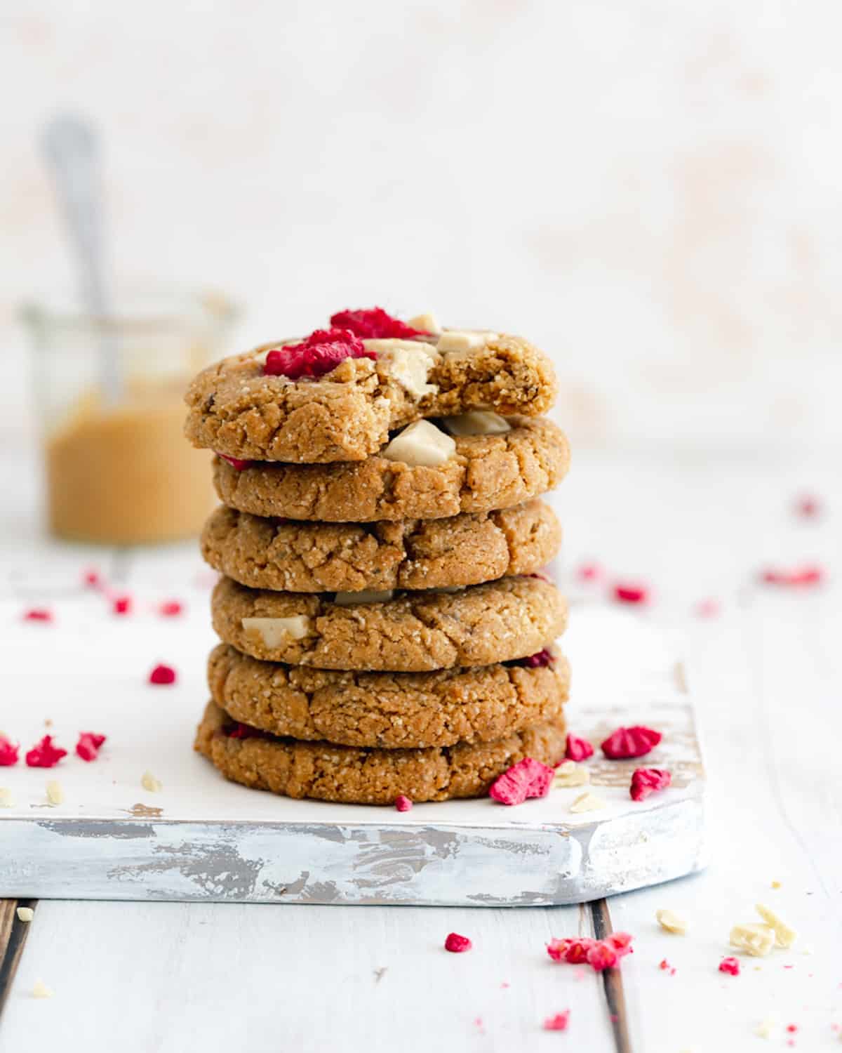 stack of white chocolate chip cookies with raspberries on a white washed wooden chopping board.