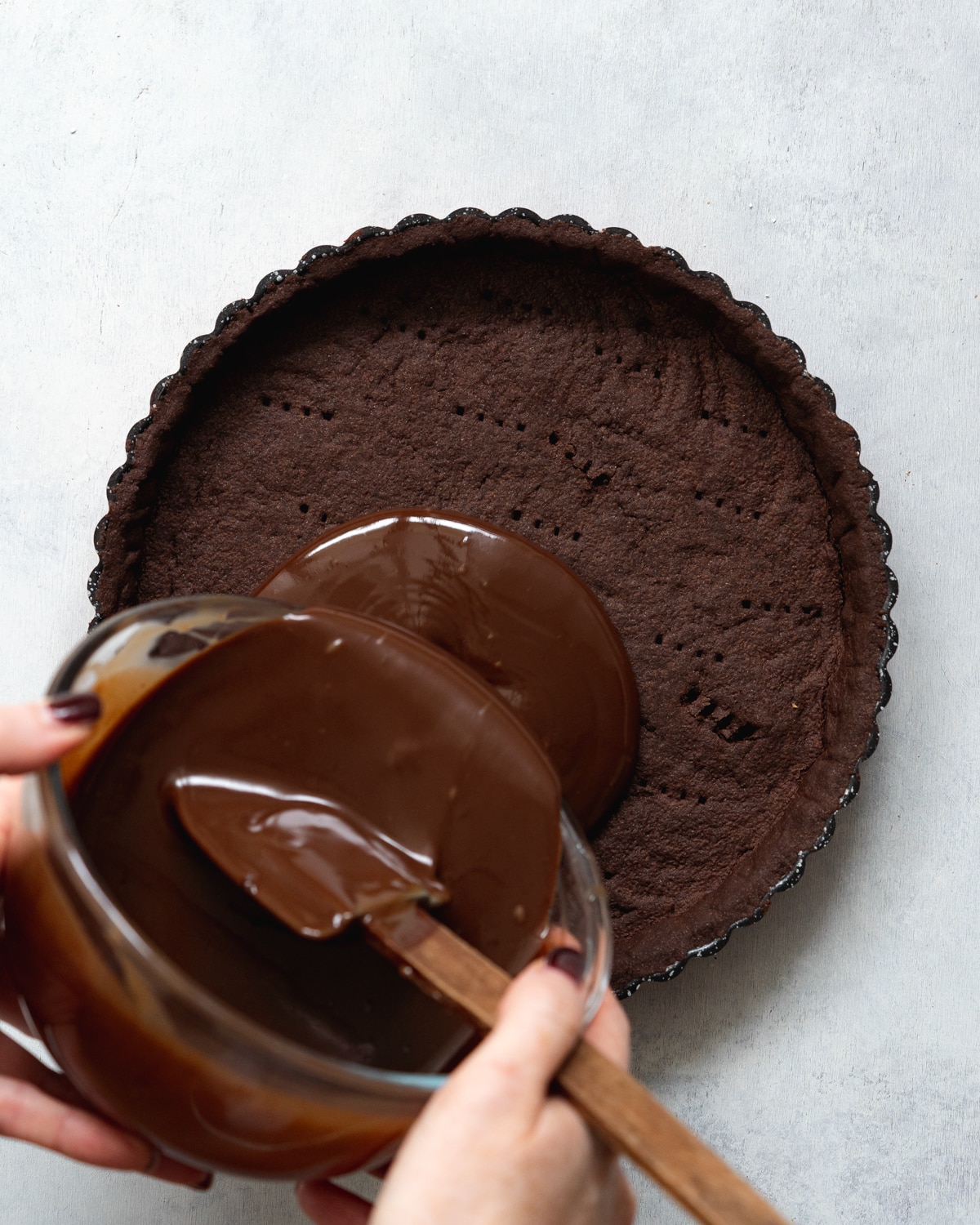 pouring chocolate ganache into a chocolate pastry shell.