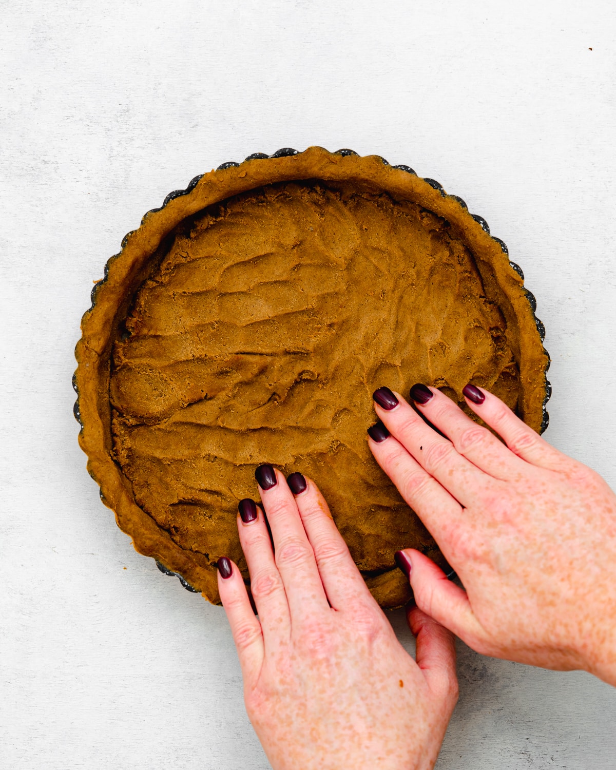 hands pressing gingerbread crust into a tart tin.