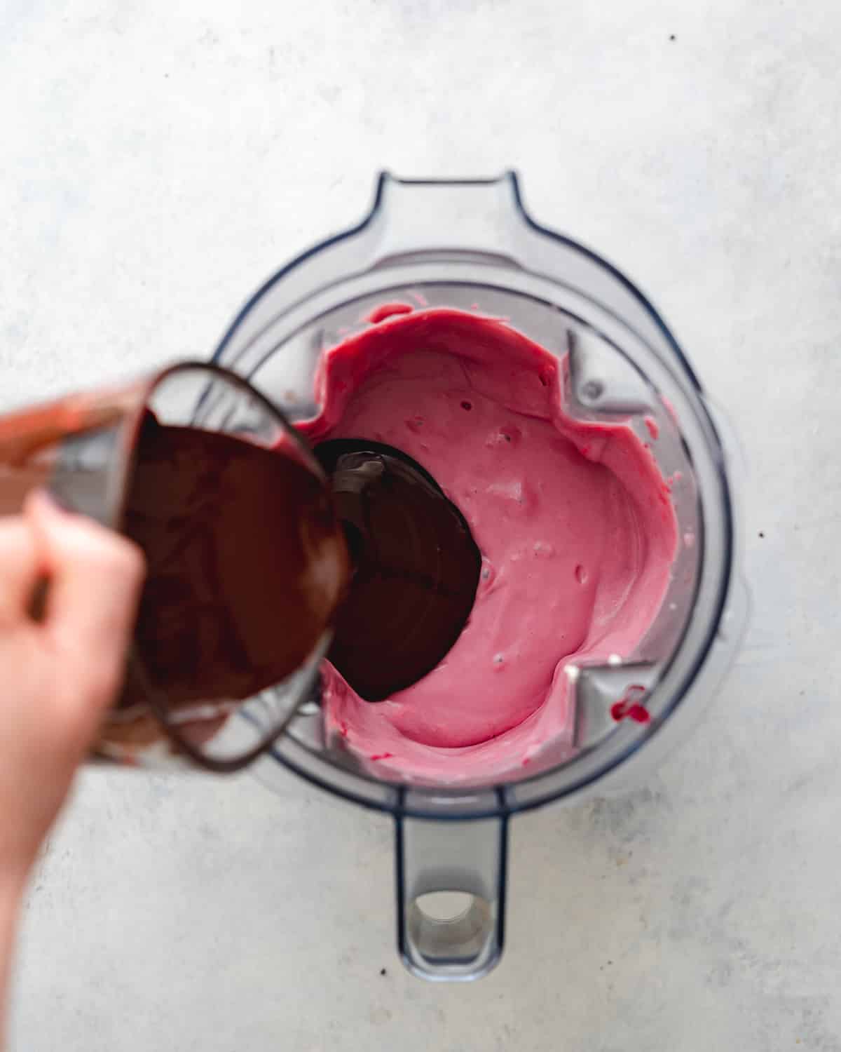 pouring melted chocolate into a blender with cherry cheesecake filling in it.