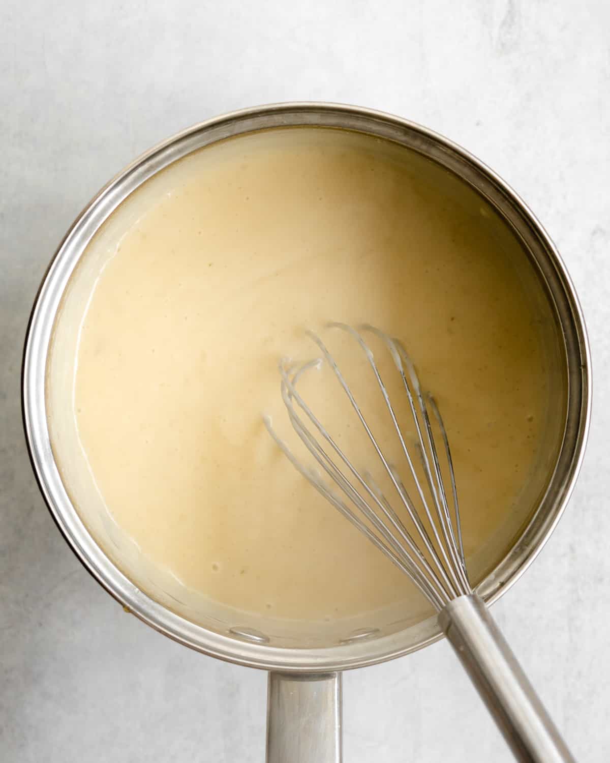 custard for creme brulee in a saucepan with a whisk in it.